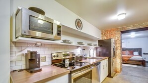 A modern kitchen with a coffee machine, microwave, oven, and dishwasher. There is a brick wall and a bed visible in the background. - Dtwn Knoxville Studio Half-mi to Market Square! (Knoxville)