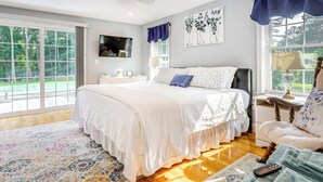 Une chambre avec un grand lit, un bureau et une chaise. Il y a une fenêtre donnant sur un paysage verdoyant.