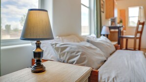A neatly made bed with white linens, a wooden bedside table with a lamp, and a view of the outdoors through a window. - Las Cruces Studio ~ 3 Mi to Nmsu! (Las Cruces)