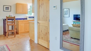 A modern kitchen with wooden cabinets, a wooden door, and a visible thermostat. - Las Cruces Studio ~ 3 Mi to Nmsu! (Las Cruces)
