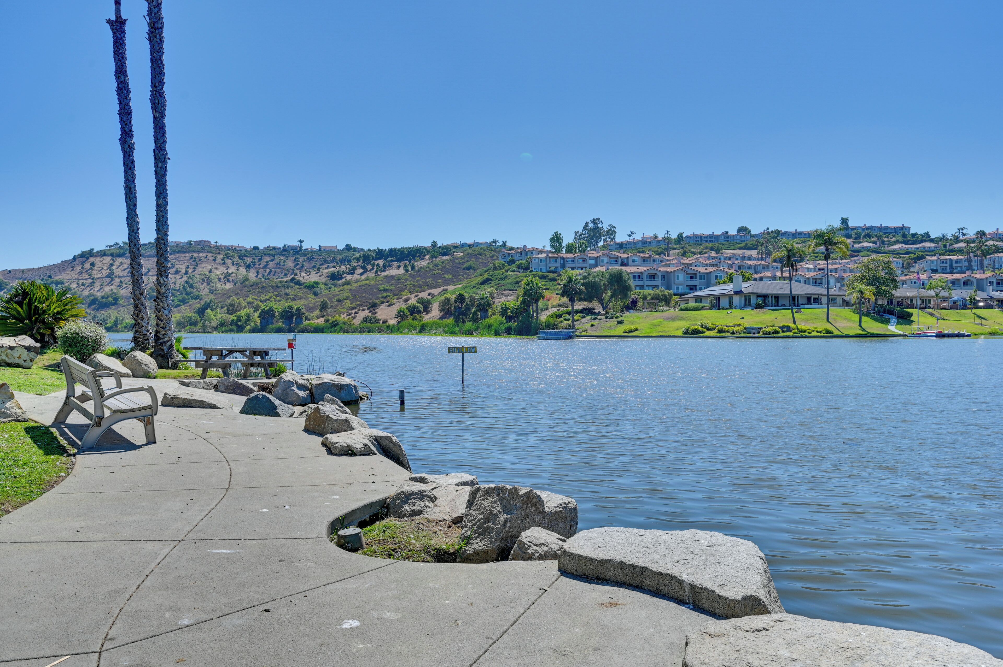 A lakeside walkway with benches, a picnic table, and a sign indicating a viewpoint.
