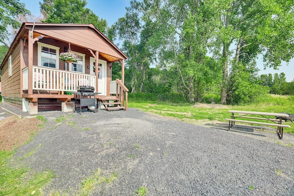 A wooden cabin with a porch, a grill, and a picnic table.