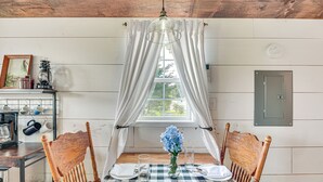 A dining area with a wooden table set for two, a vase with flowers, and a window with white curtains.