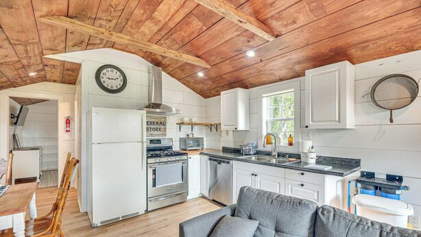 A kitchen with white cabinets, a stove, and a dishwasher. There is a gray sofa with a pillow in the living area.