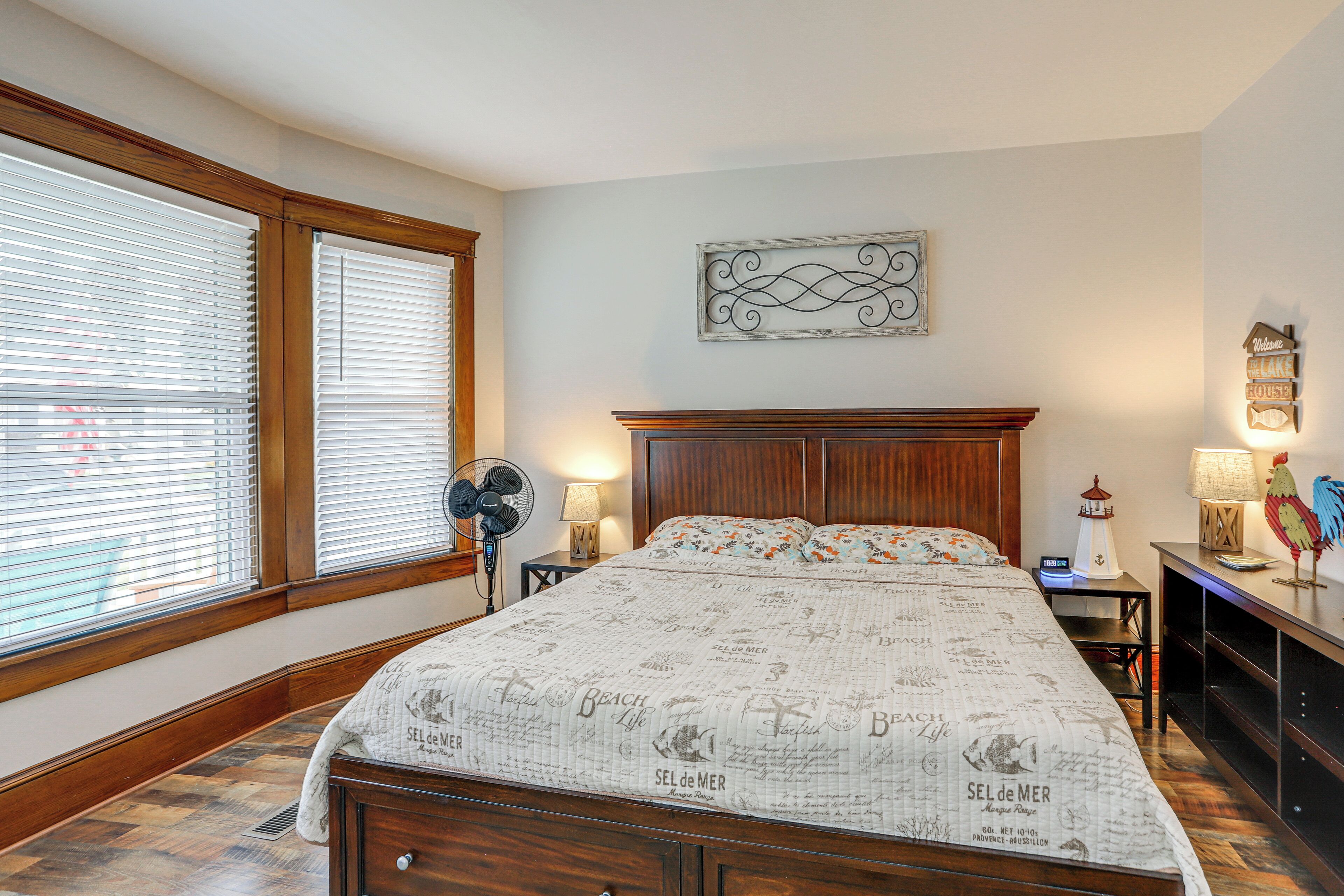 A bedroom with a large bed, wooden headboard, a wall-mounted artwork, and a nightstand with a lamp.