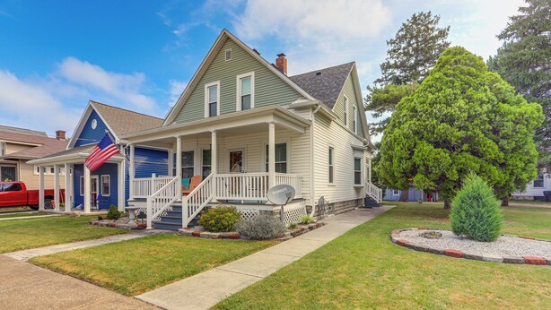A two-story house with a front porch, a small front yard, and a large tree.