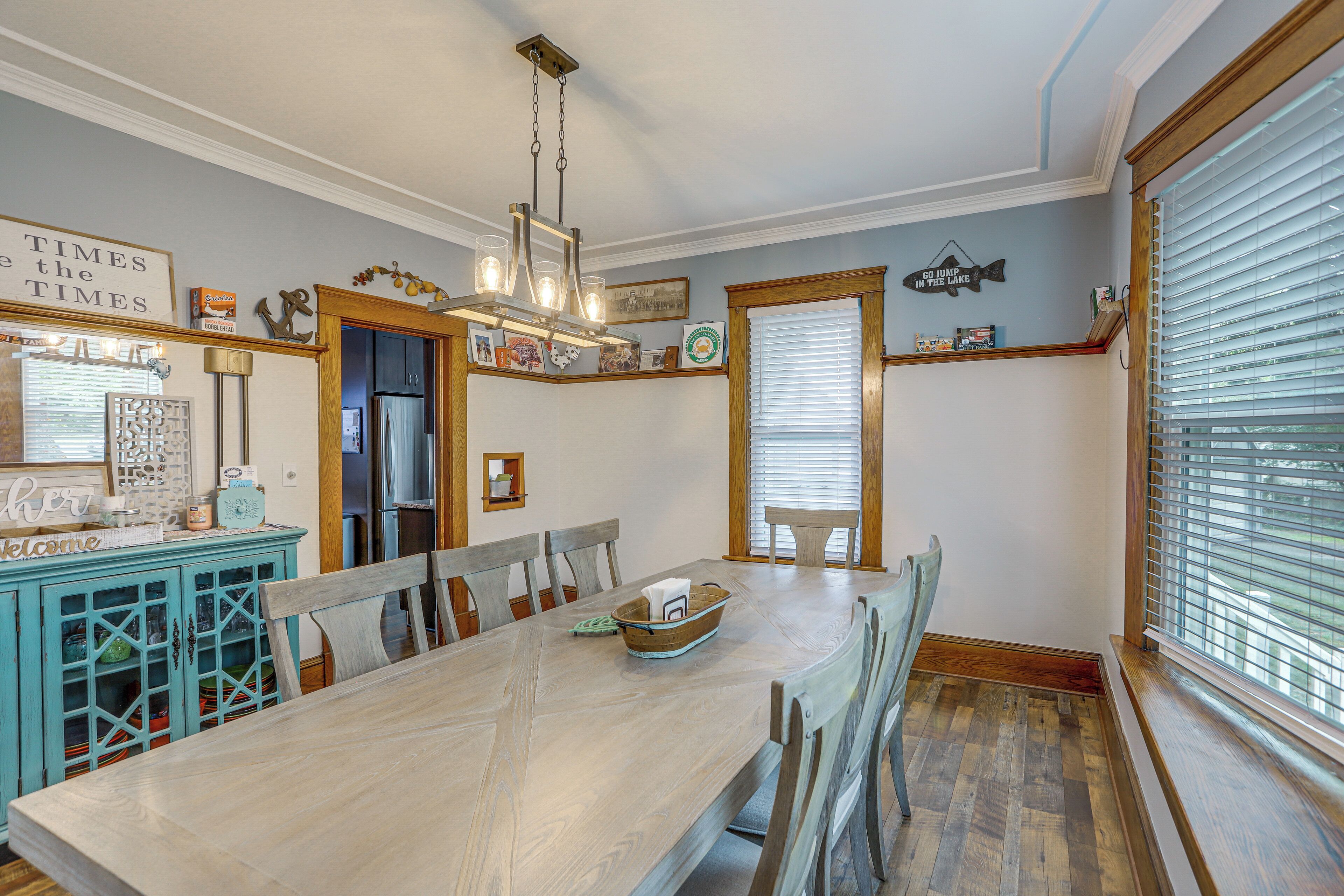 A dining area with a wooden table, chairs, and a chandelier. There is a window with blinds and a door leading to another room.