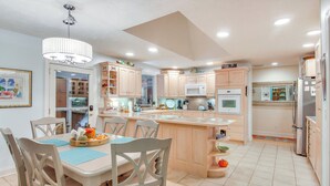 A spacious kitchen with a central island, wooden cabinetry, and a dining area with chairs and a table. - Blue Ridge Mtn Retreat: Porches & Creek Access (Hendersonville)