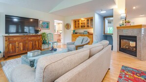 A spacious living room with a large flat-screen TV, a wooden cabinet, a sofa, and a fireplace. - Blue Ridge Mtn Retreat: Porches & Creek Access (Hendersonville)