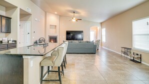 A spacious kitchen with a central island, a dining area with bar stools, a large flat-screen TV, and a ceiling fan. - Santa Teresa Home w/ Patio & Grill! (Santa Teresa)