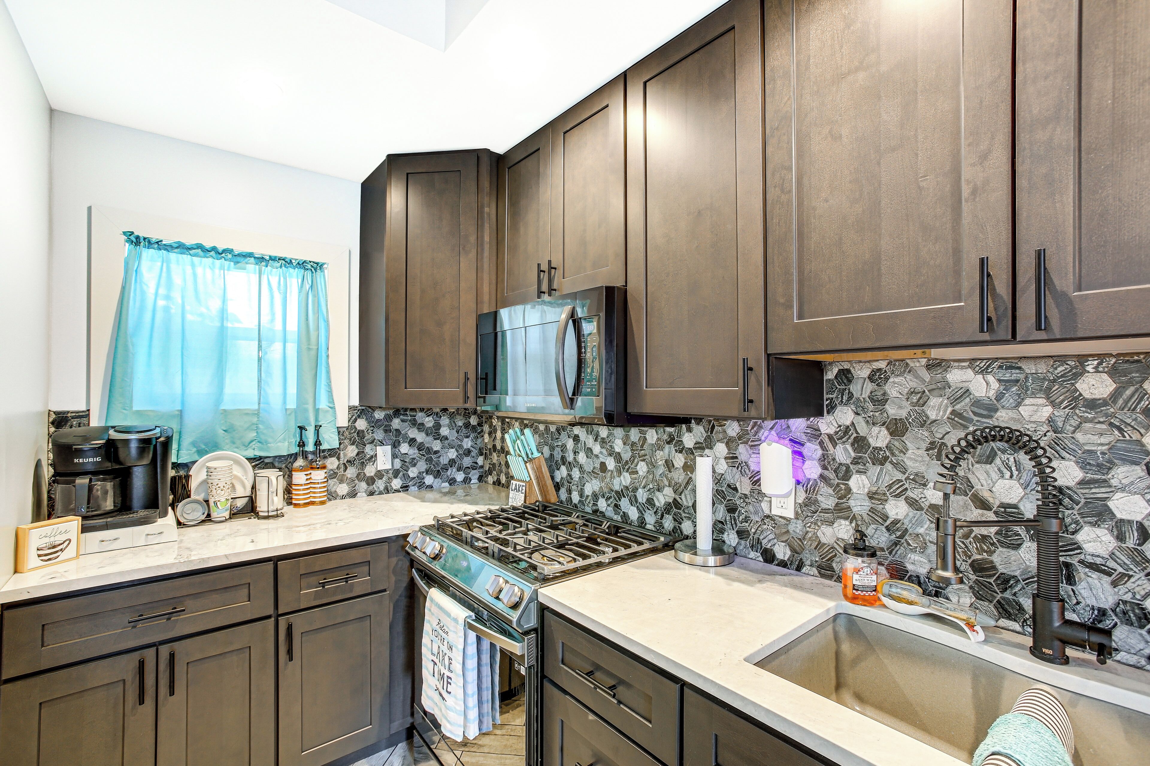 A kitchen with dark wooden cabinets, a stainless steel range, a microwave, and a tiled backsplash.