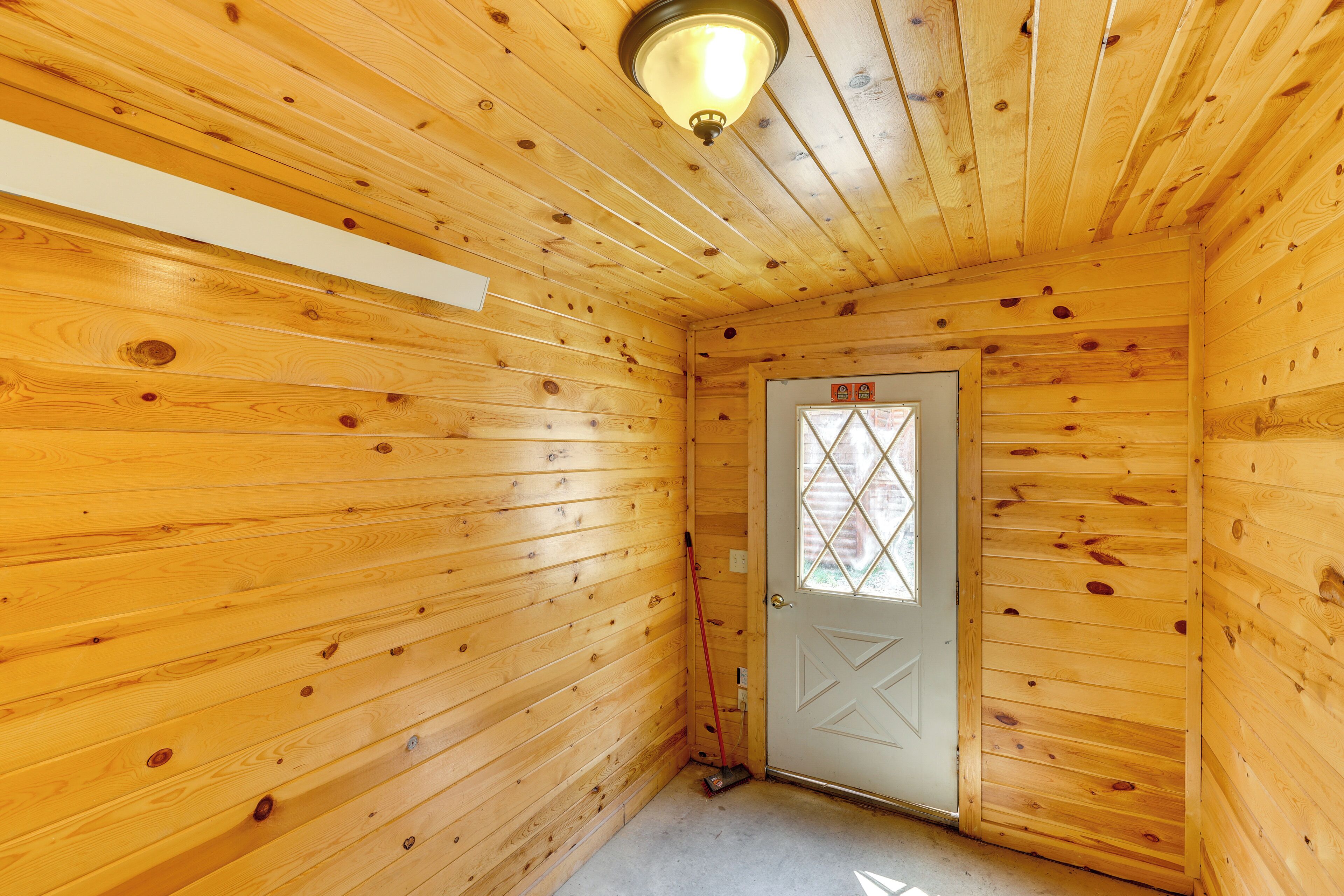 A wooden interior with a door, a light fixture, and a white wall.