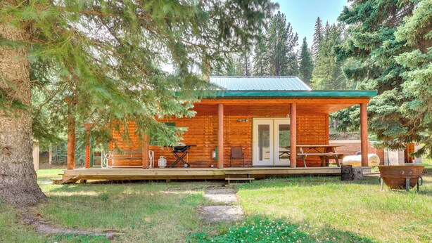 Een houten chalet met een overdekte veranda, een eettafel en een barbecue buiten.