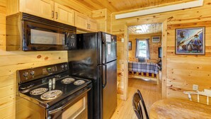 Een houten chalet van binnen, met een keukenhoek met een fornuis, magnetron en koelkast.