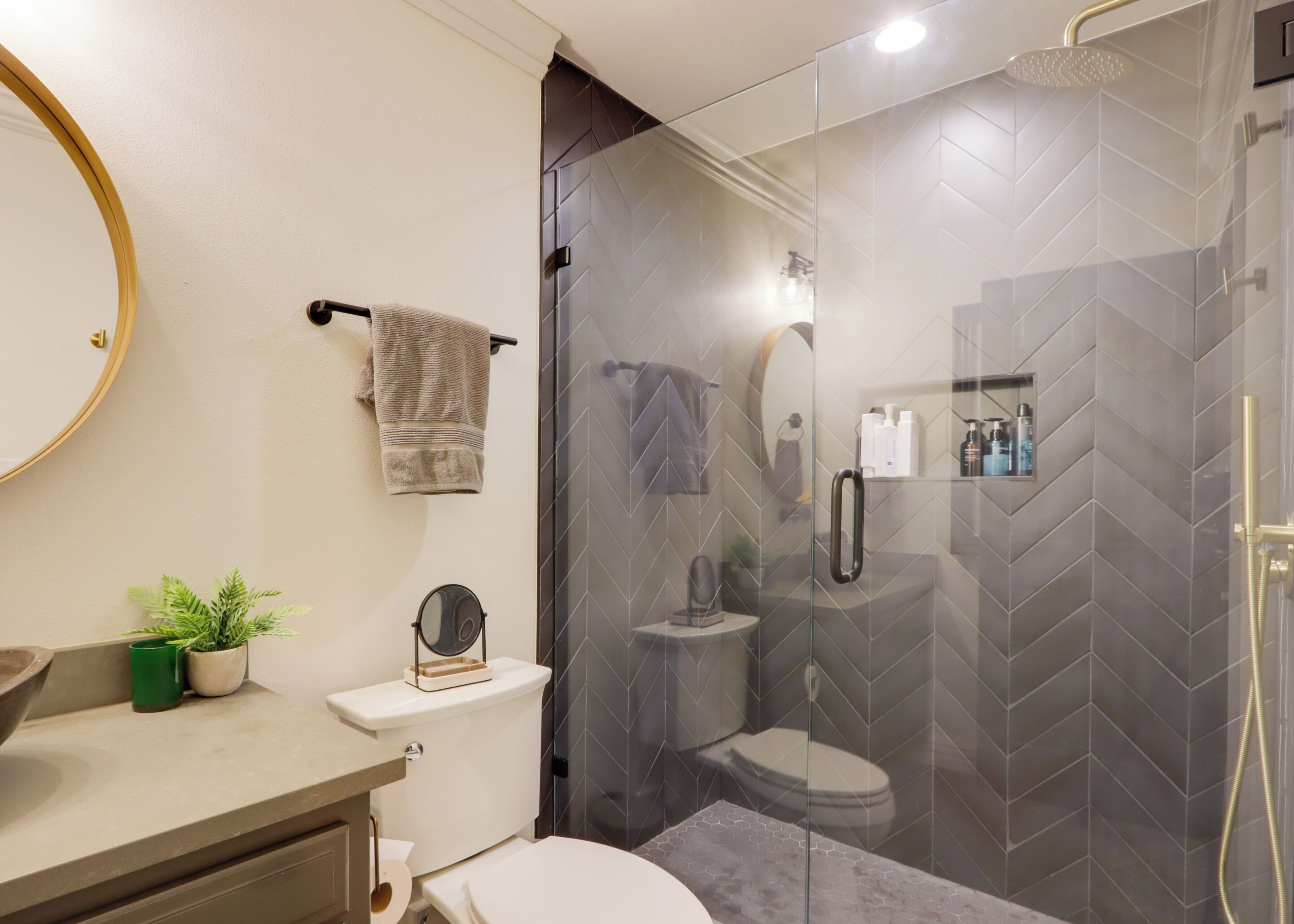 Un baño moderno con ducha de vidrio, inodoro, lavamanos con espejo y toallero.