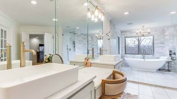 Un baño moderno con una amplia bañera independiente, un tocador doble con detalles dorados y un espejo grande.
