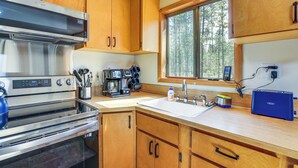 Una cocina con armarios de madera, una campana extractora de acero inoxidable, una cafetera y un ventanal con vistas a árboles.