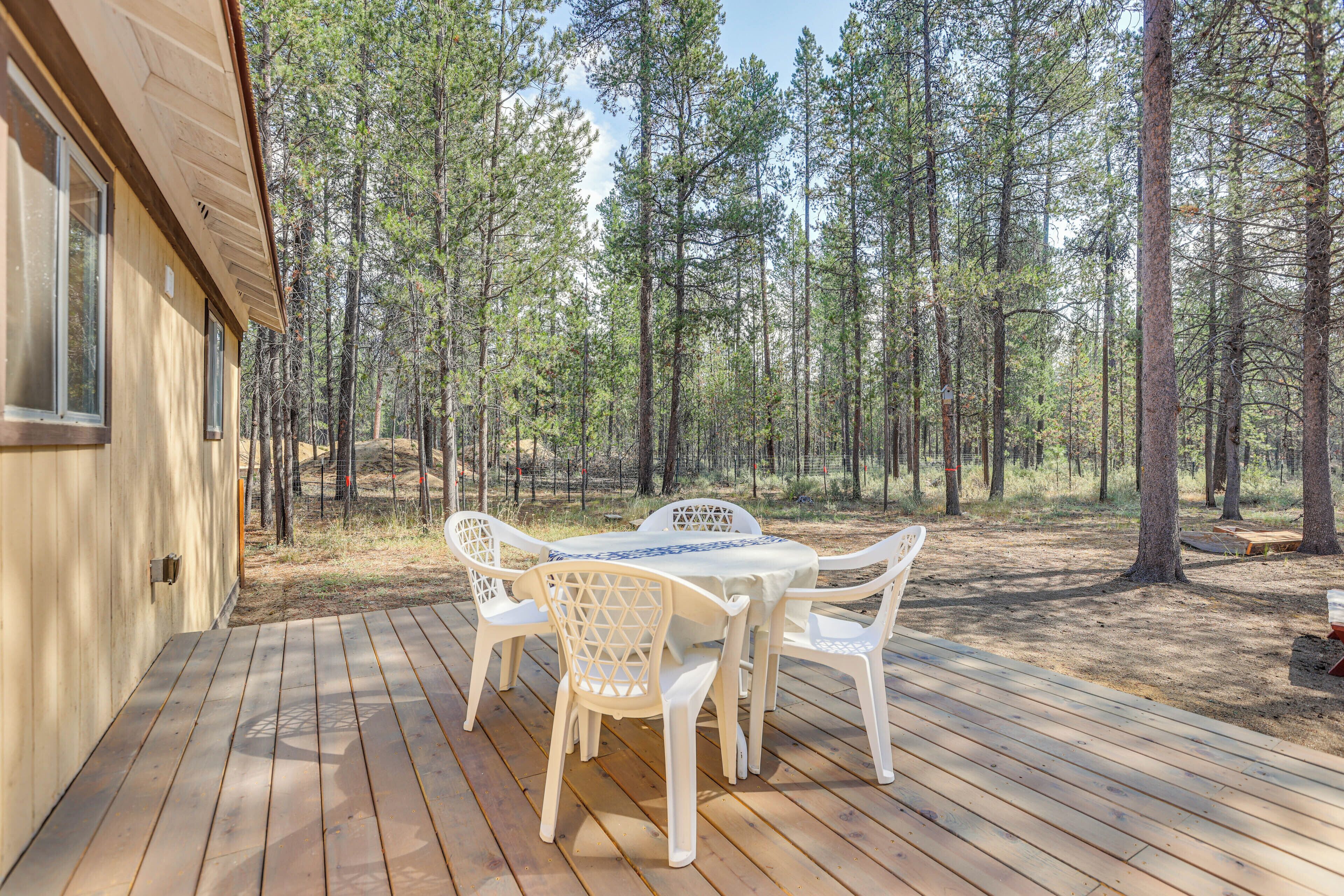 A wooden deck with a table and chairs, surrounded by a forest.