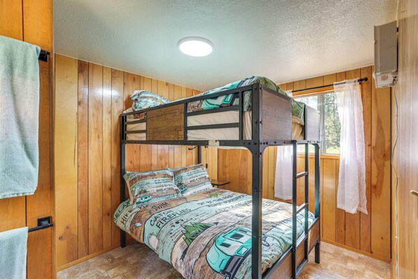 Una cama litera con una colcha estampada, paredes de madera, una ventana con cortinas y una lámpara en el techo.