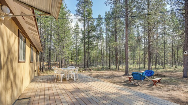 Una terraza de madera con una mesa y sillas, rodeada de un bosque.