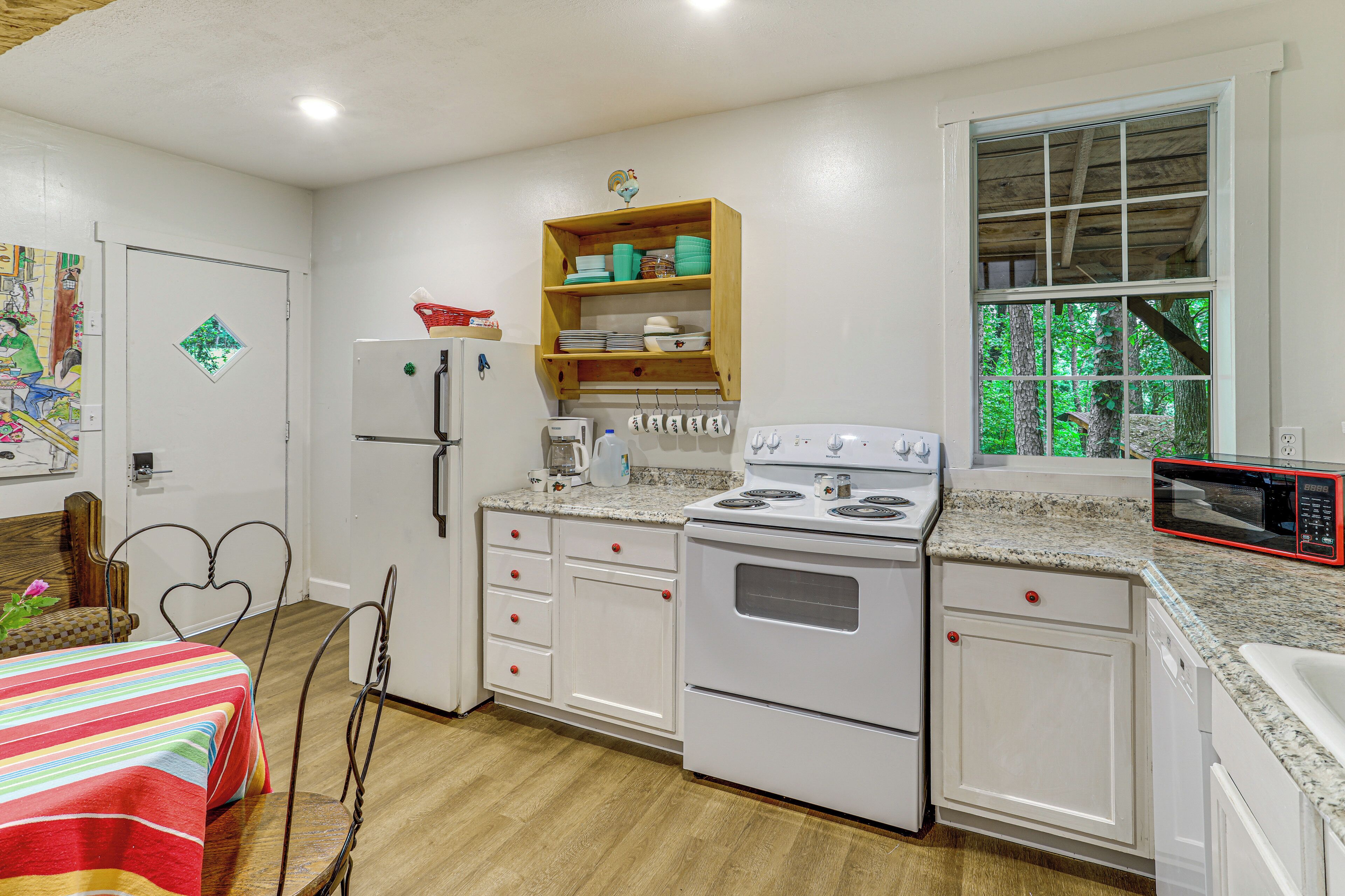 A kitchen with white cabinets, a stove, a microwave, and a window with a view of trees.