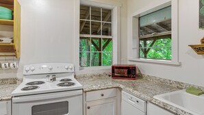 A kitchen with a white stove, a microwave, and a sink. There are windows with views of trees. - Mountain View Cabin: Music, Crafts & Shopping! (Mountain View)