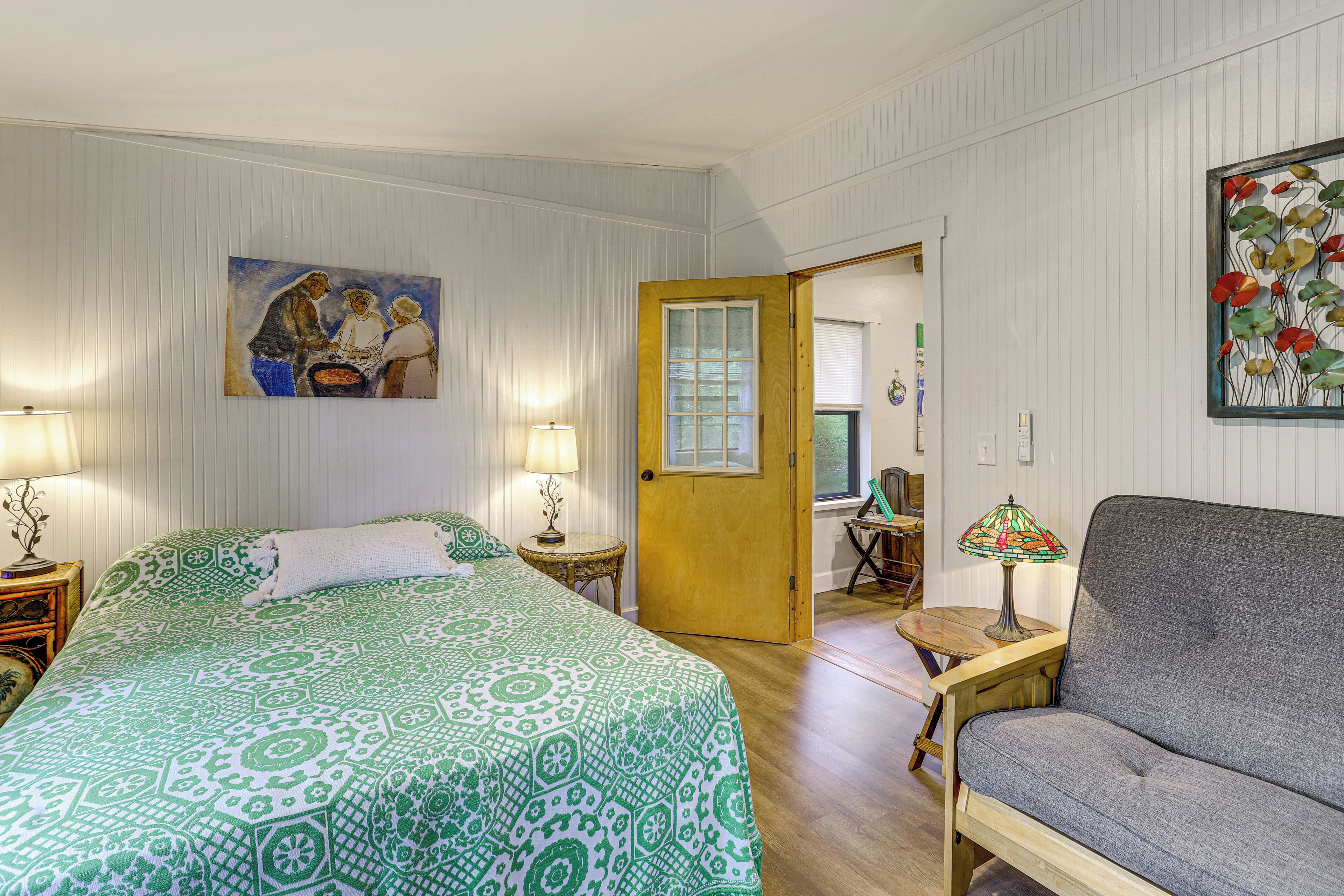 A room with a bed, a sofa, a door, a lamp, and a painting on the wall.