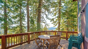 A wooden deck with a table and chairs, surrounded by tall trees and a view of the mountains. - Deck w/ Mountain Views: Cabin in Bear Valley! (Arnold)