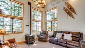 A cozy living room with a fireplace, leather furniture, large windows, and a forest view. - Deck w/ Mountain Views: Cabin in Bear Valley! (Arnold)