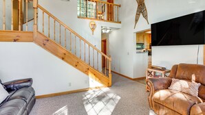 A spacious living area with a wooden staircase, a leather sofa, a brown armchair, and a flat-screen TV. - Deck w/ Mountain Views: Cabin in Bear Valley! (Arnold)
