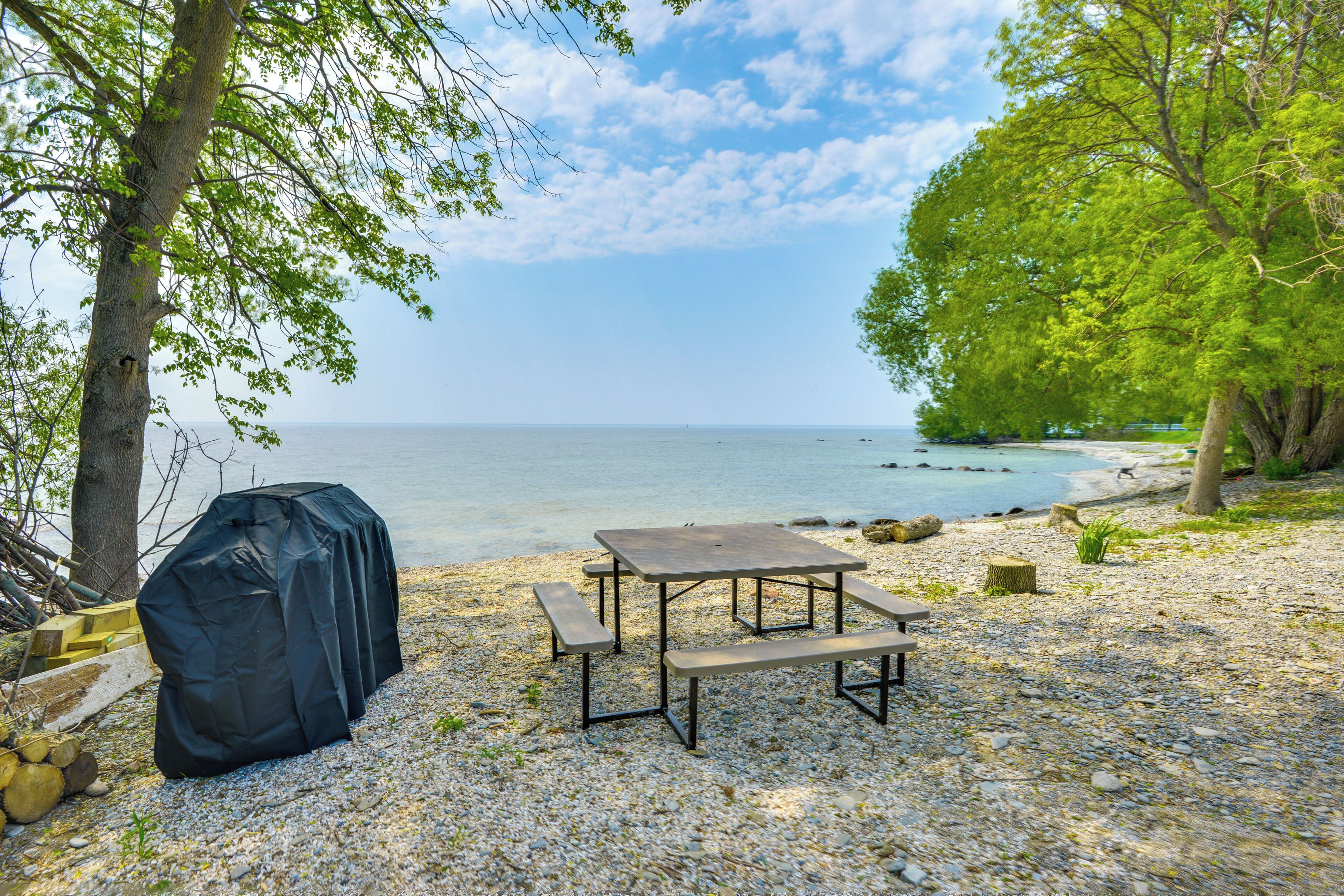 Ein Picknicktisch und ein Grill an einem kiesigen Strand mit Bäumen und Blick auf das Meer.