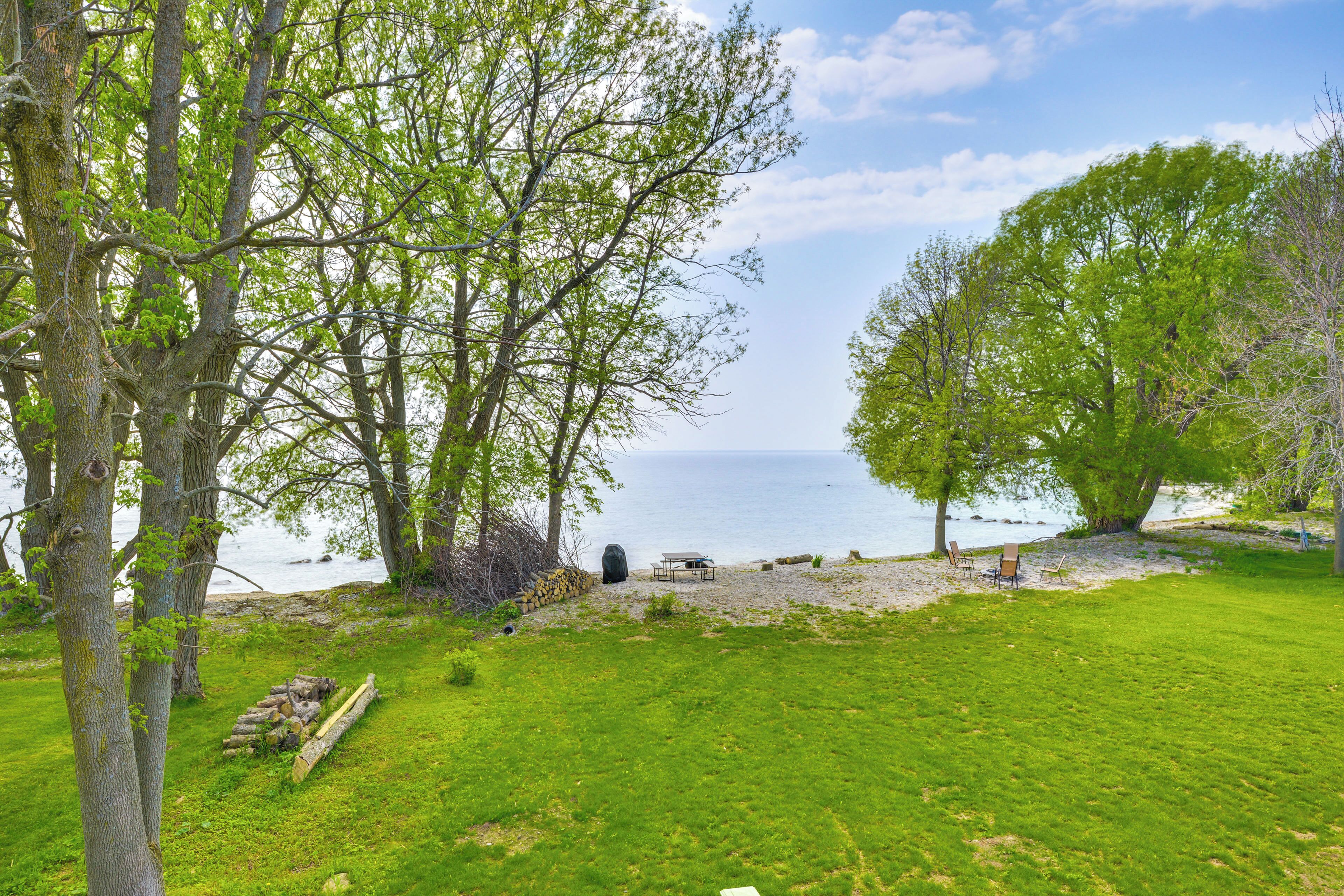 A grassy area with a table and chairs near a body of water, surrounded by trees.