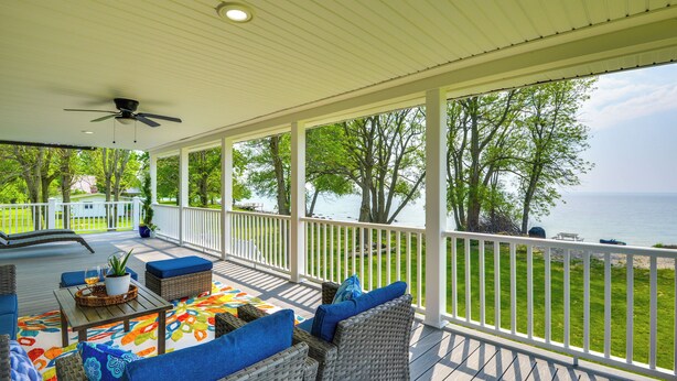 Eine überdachte Terrasse mit Korbmöbeln, einem Deckenventilator und Blick aufs Wasser.