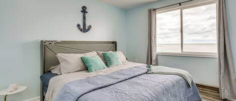 A bedroom with a bed, a nightstand, a window with curtains, and a wall-mounted anchor decoration.