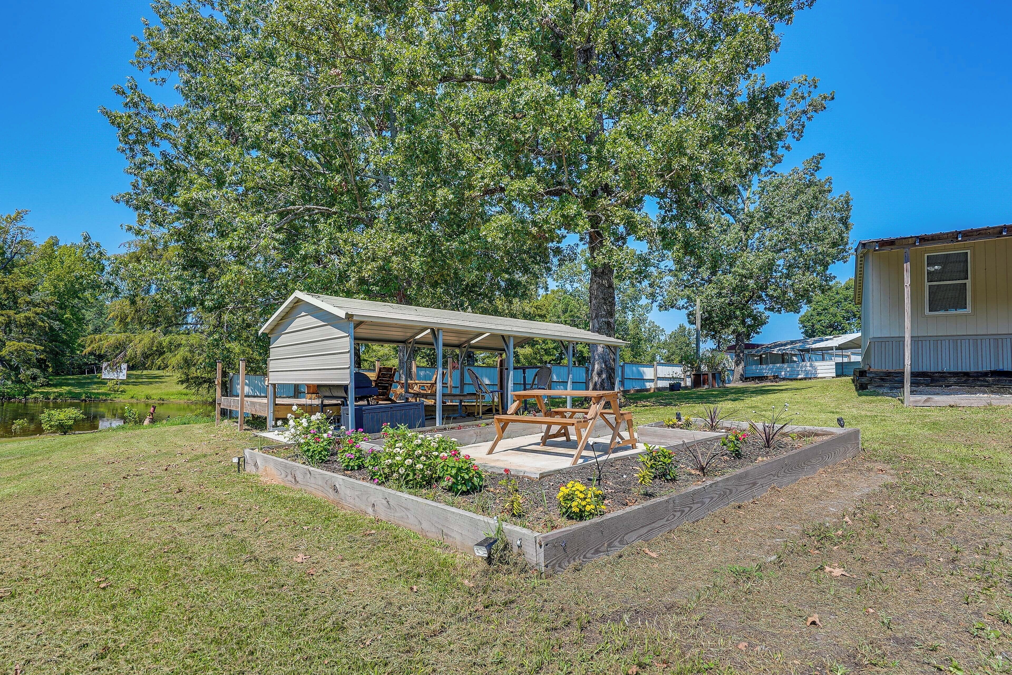A covered outdoor seating area with a picnic table, surrounded by raised garden beds with various plants.