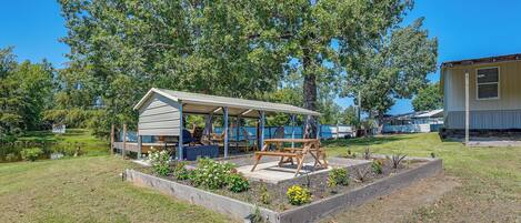 A covered outdoor seating area with a picnic table, surrounded by raised garden beds with various plants.