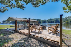 A wooden deck with picnic tables and chairs, a covered seating area, and a view of a lake. - Waterfront Buster's Place on Hickory w/ Fire Pit (Many)