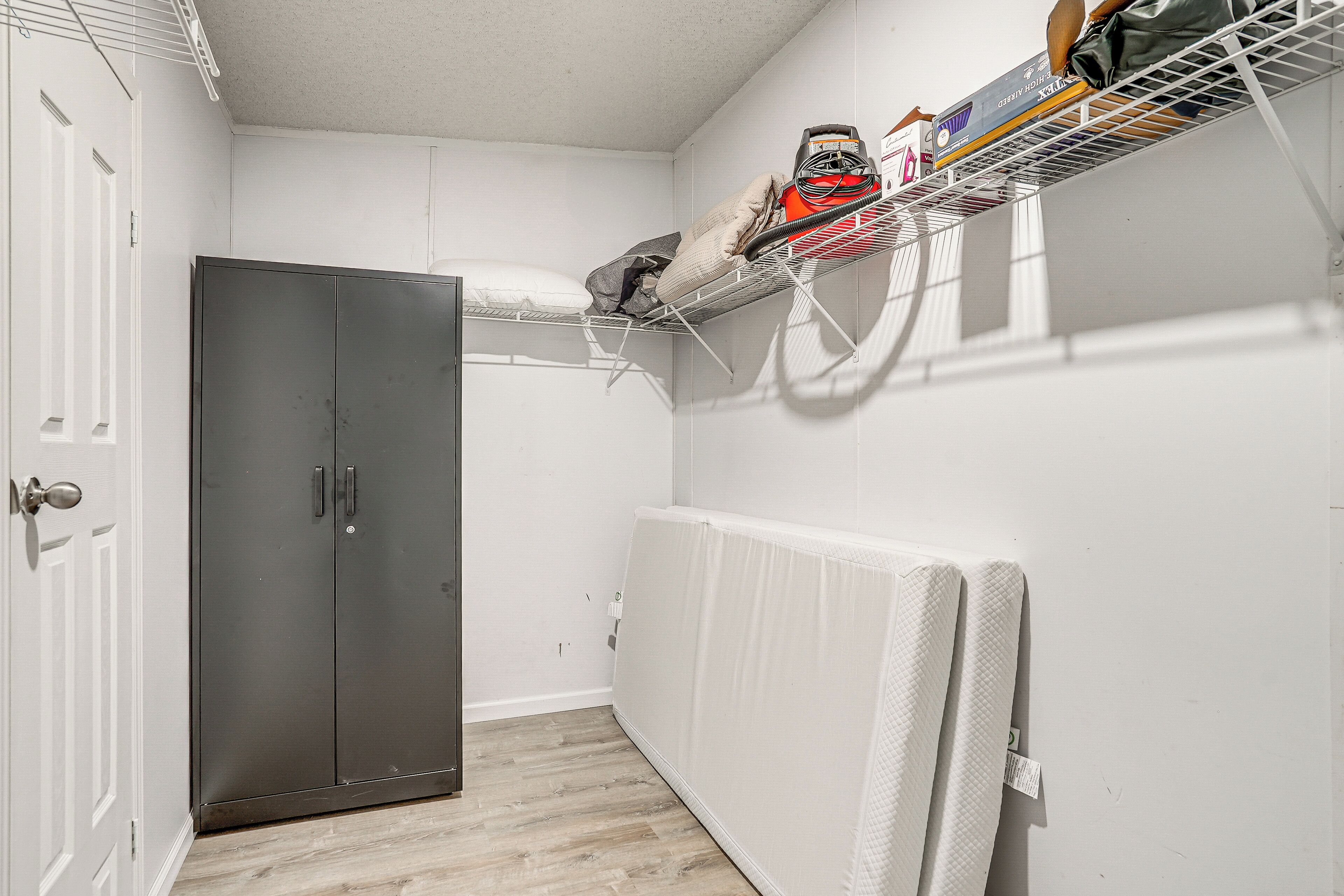 Una habitación pequeña con un armario, un radiador y una estantería con distintos objetos.