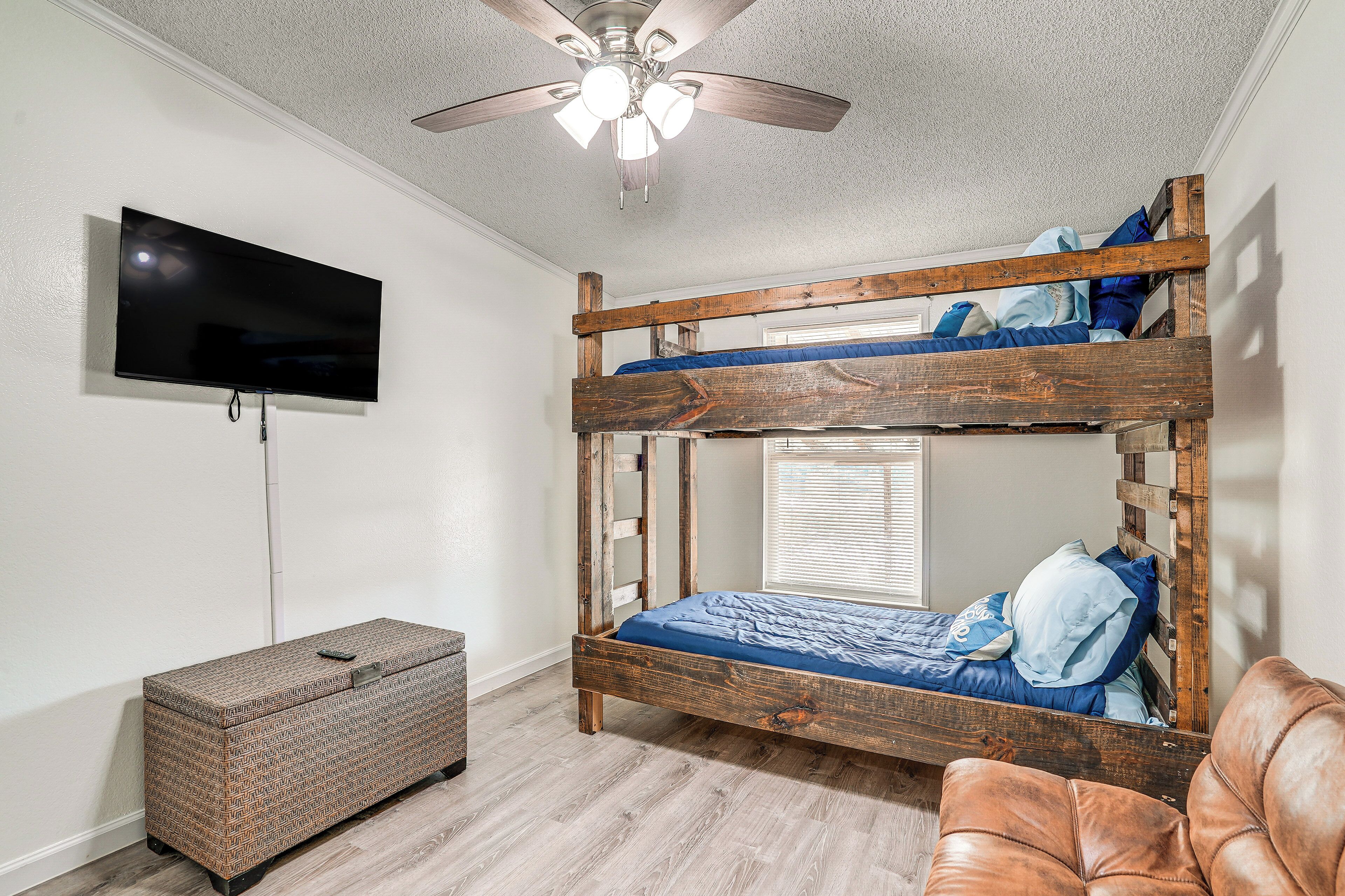 A bunk bed with a television mounted on the wall, a ceiling fan, and a leather chair.