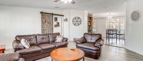 Ein geräumiges Wohnzimmer mit Ledersofas, einem runden Couchtisch und einem Deckenventilator.