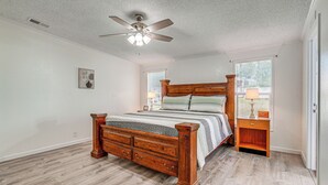 Un dormitorio con cama de madera, mesita de noche, ventilador de techo y ventana con persianas.