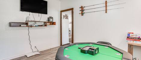 A room with a green pool table, a flat-screen TV mounted on the wall, and a wooden shelf with various items.