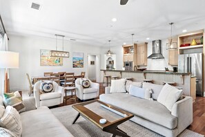Una sala moderna con un sofá, sillas y una mesa de centro. Cuenta con una zona de cocina con armarios y electrodomésticos.