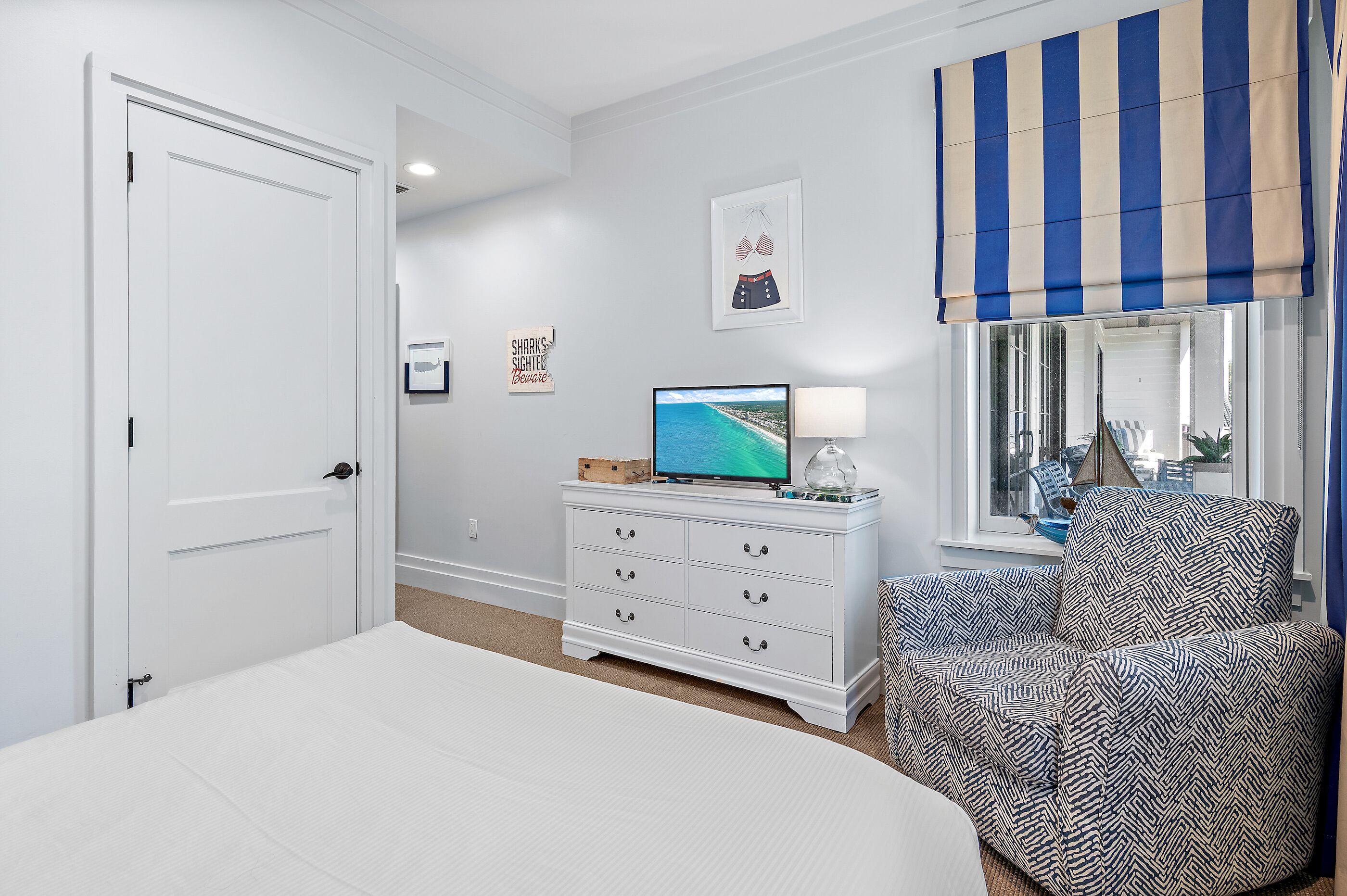 Une chambre à coucher avec un lit, une commode, un téléviseur et une fenêtre avec un rideau à rayures.