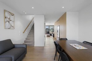 Un intérieur moderne comprenant un escalier, un coin repas avec une table et des chaises en bois, et un salon avec un canapé.