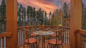 A wooden deck with a glass table and chairs, surrounded by a railing, overlooking a forested area. - Short Walk to Ski Lifts | Boulder Ridge Retreat (Breckenridge)