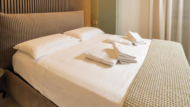 A modern hotel room with a large bed, a wooden panel wall, and a view of the city through the window. - Ypnos Rooms (Naples)