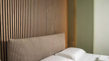 A hotel room with a wooden slat headboard, a bed with white linens, and a plain wall.