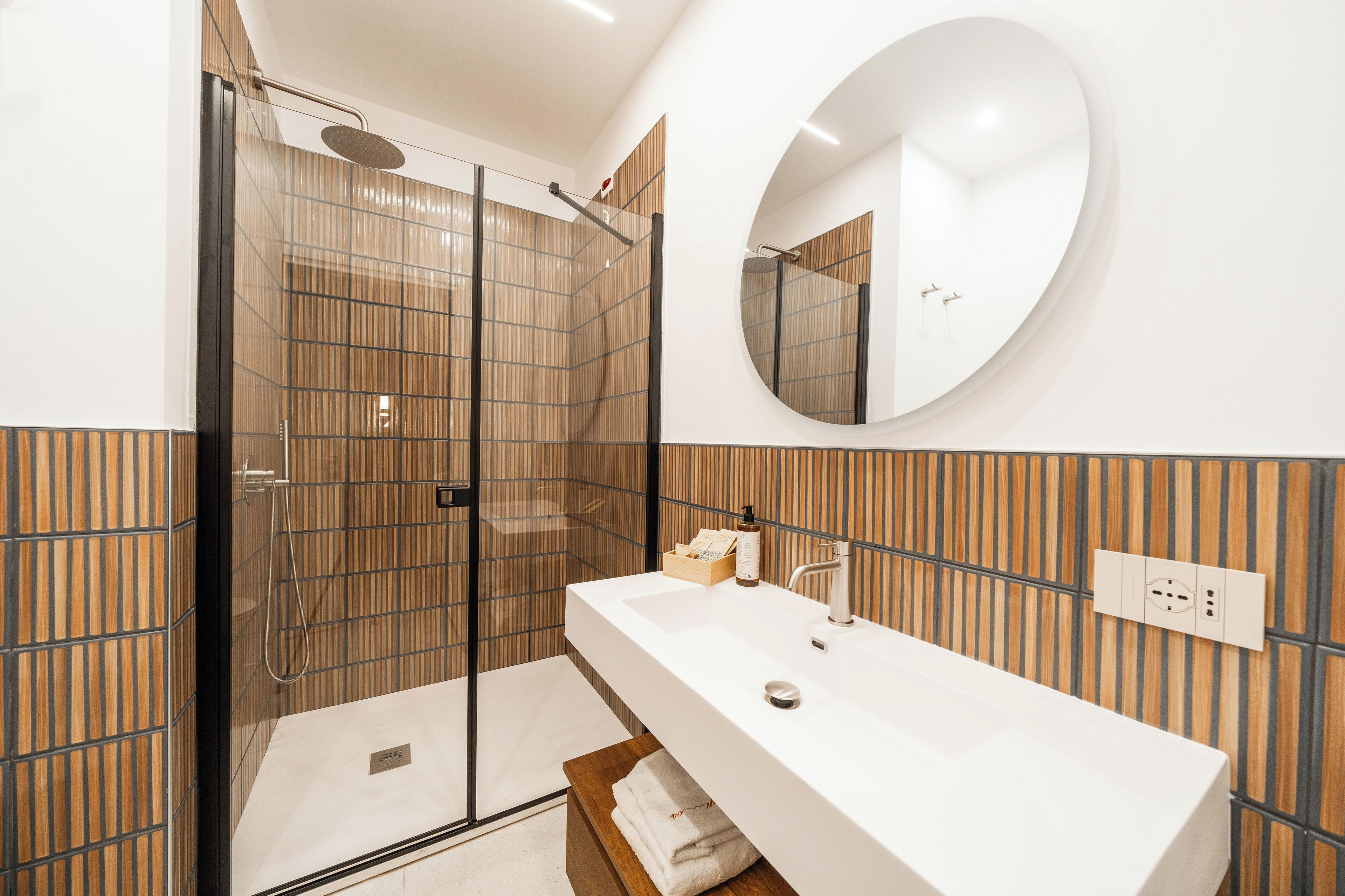 A modern bathroom with a glass-enclosed shower, a large white sink, and a mirror above it.