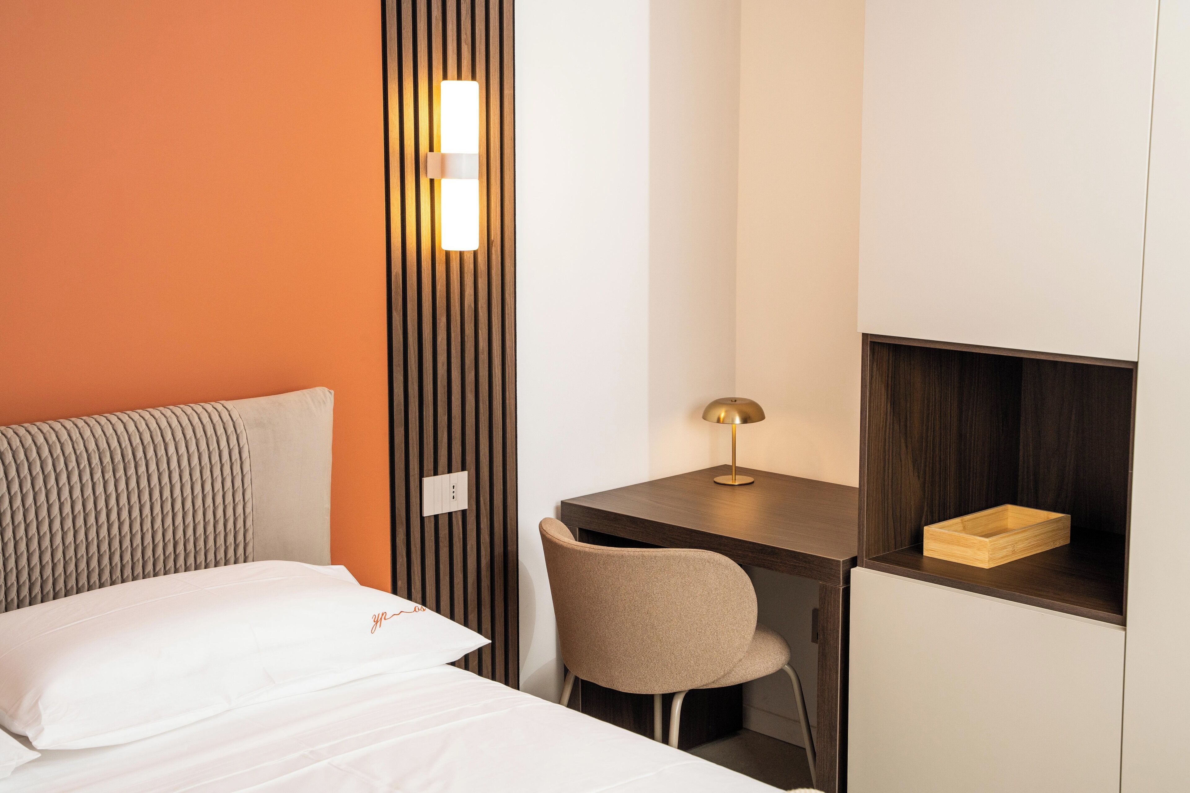 Une chambre d’hôtel équipée d’un lit, d’un bureau, d’une chaise et d’une étagère fixée au mur.